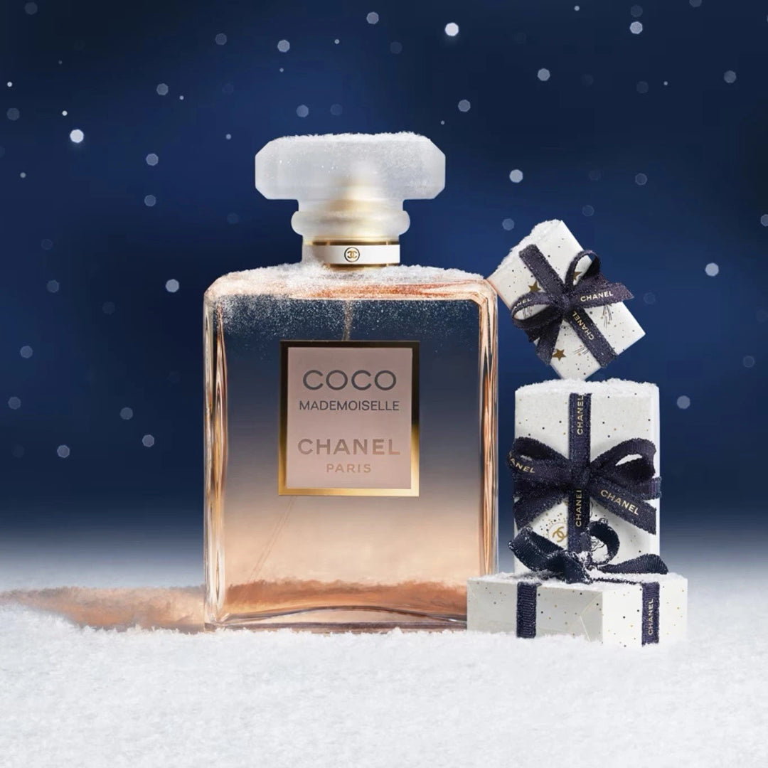 Chanel perfume bottle with two gift boxes on a snowy surface with a blue background