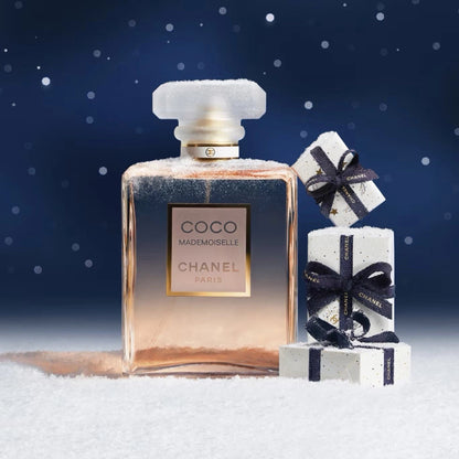 Chanel perfume bottle with two gift boxes on a snowy surface with a blue background